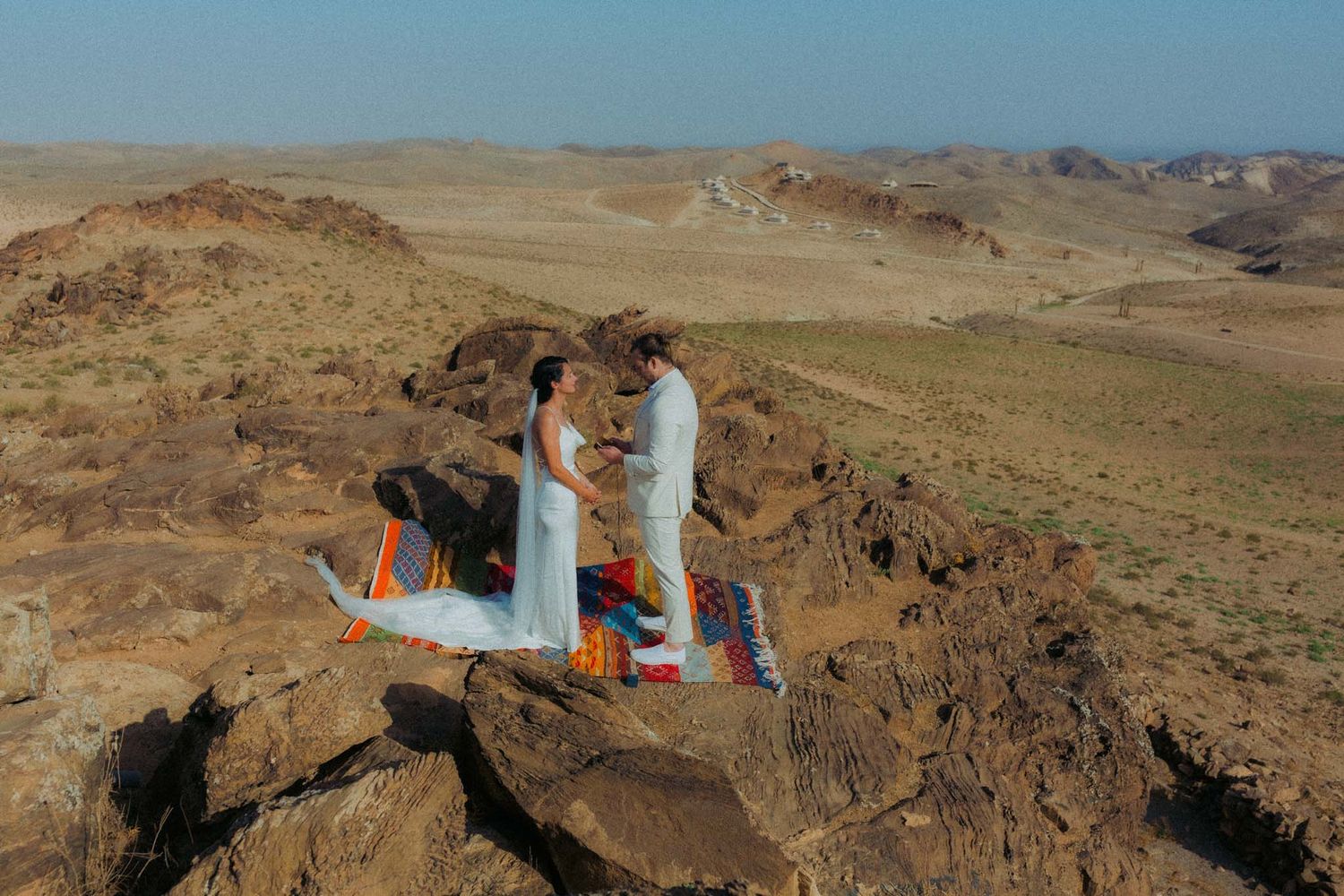 Aerial panorama showing wind turbines scattered across a rugged desert landscape with rocky outcrops and ridges.