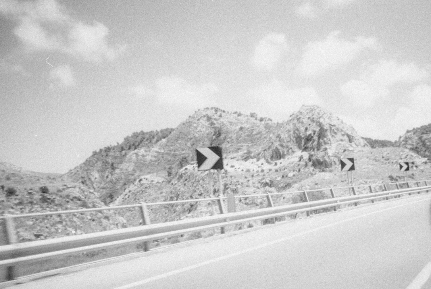 Winding mountain road with guardrails stretching into the distance under cloudy skies.