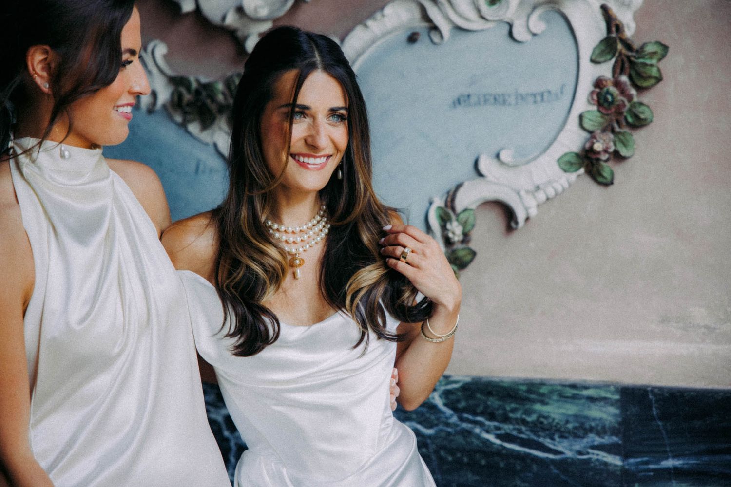 Couple in white outfits sharing romantic moments against a textured wall with floral decorations.