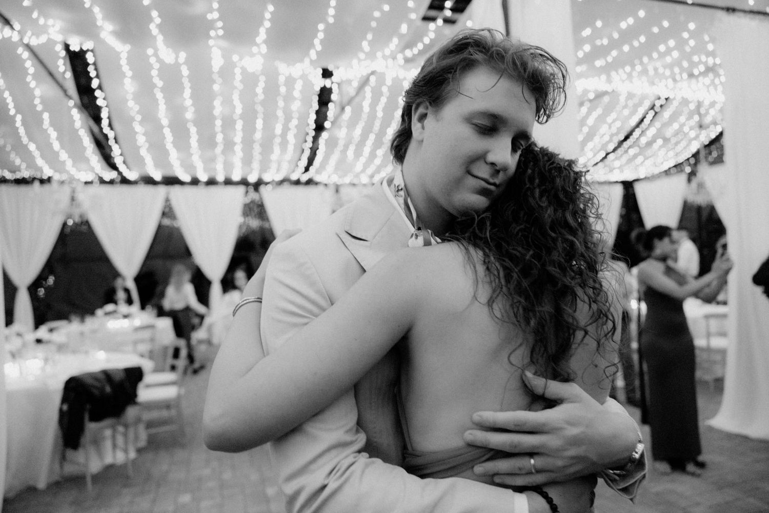 Couple dancing intimately under twinkling string lights at a wedding reception.
