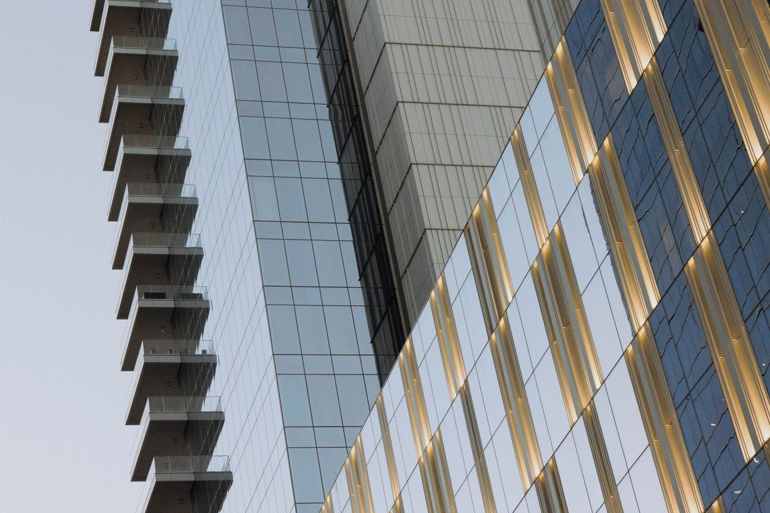 Glass and steel skyscraper facade with diagonal patterns reflecting sunlight against blue sky.