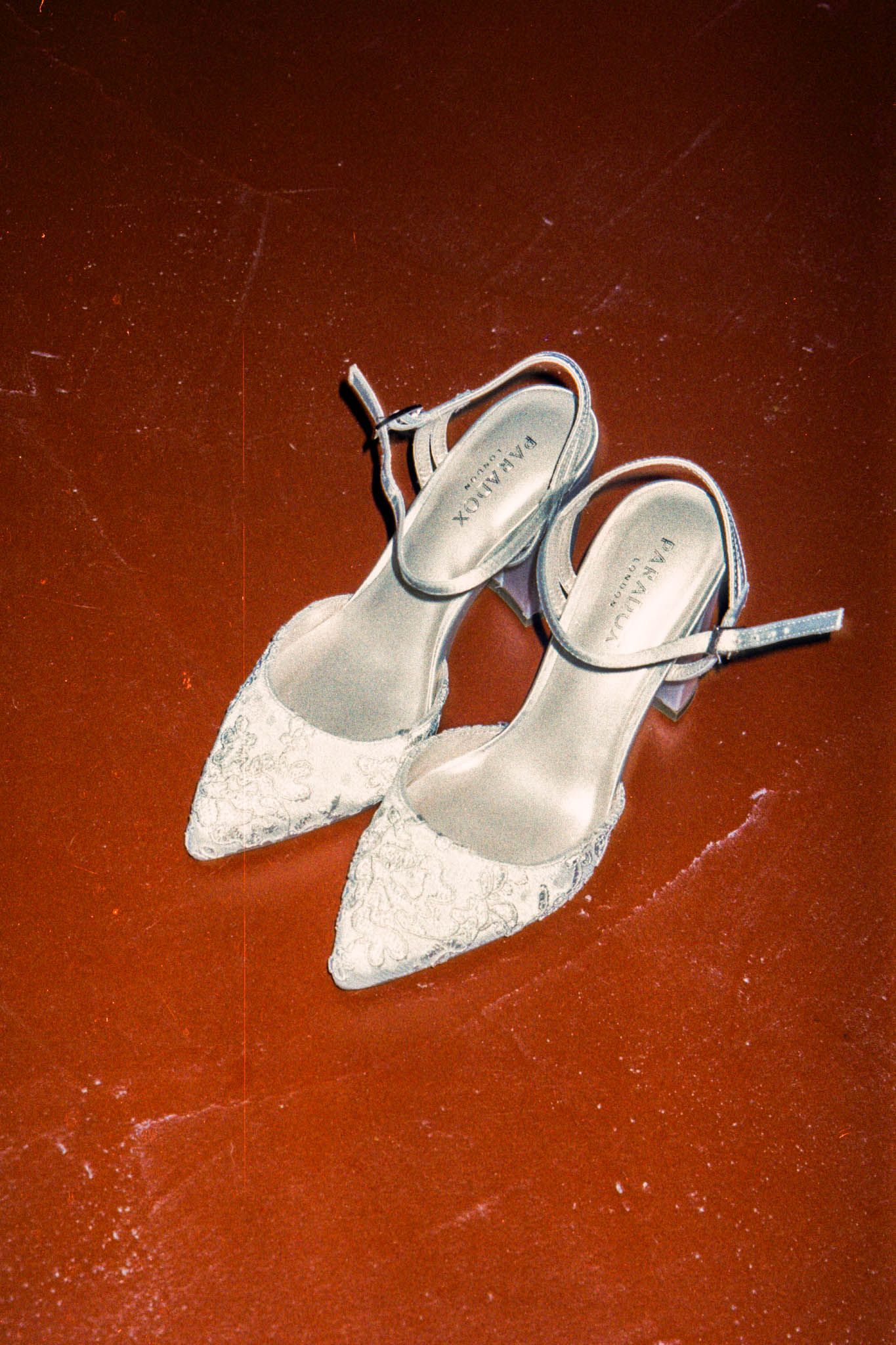 White lace bridal shoes arranged in a sequence on a dark red floor.