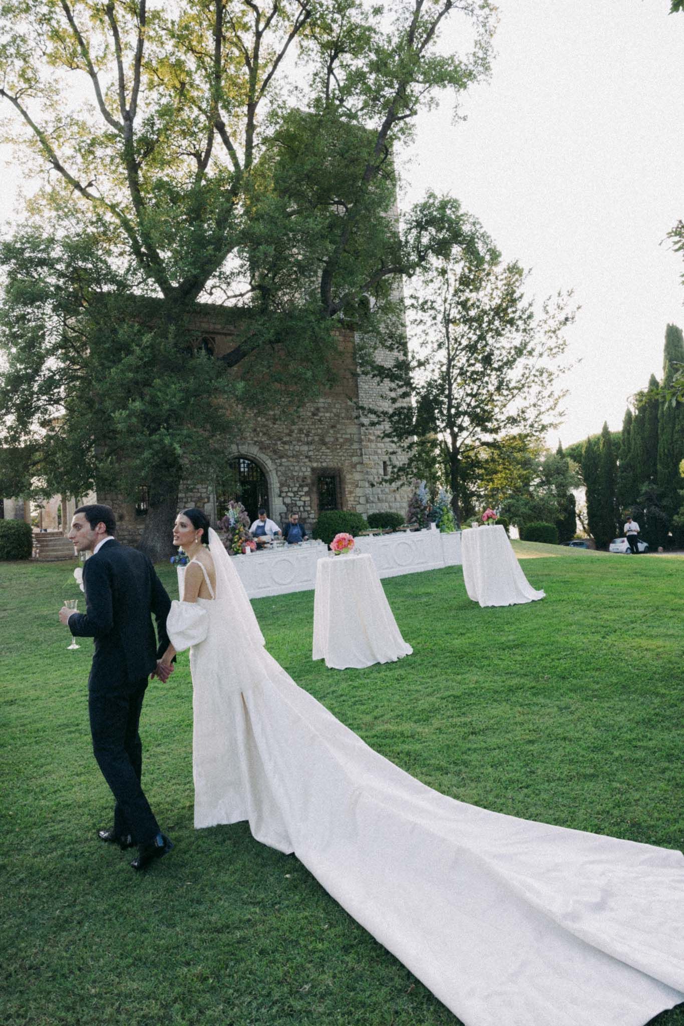 A dramatic long white wedding dress train trails across a grassy hillside garden setting at dusk.