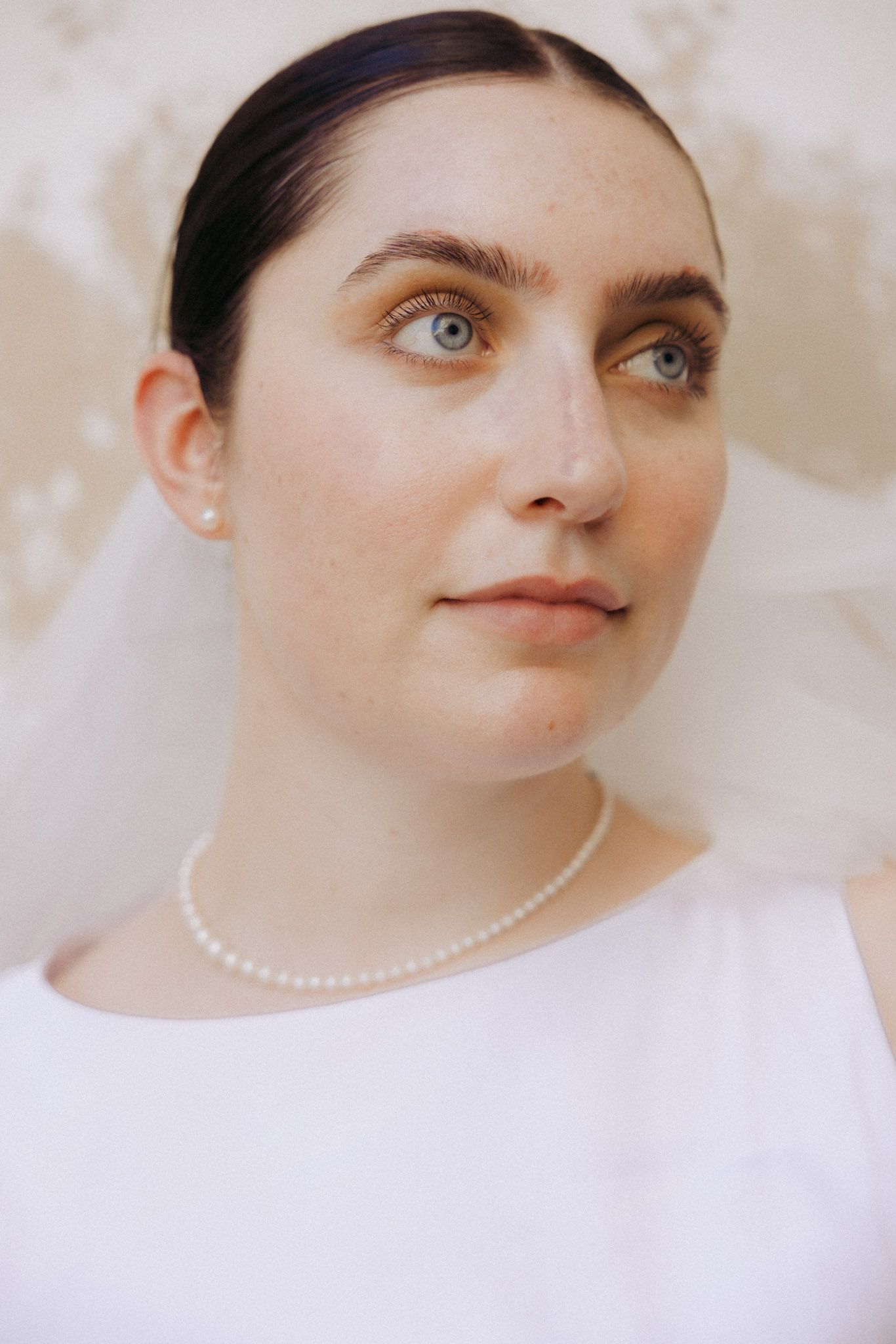 Close-up portrait of a bride wearing a white dress, pearl necklace and earrings with a delicate veil.