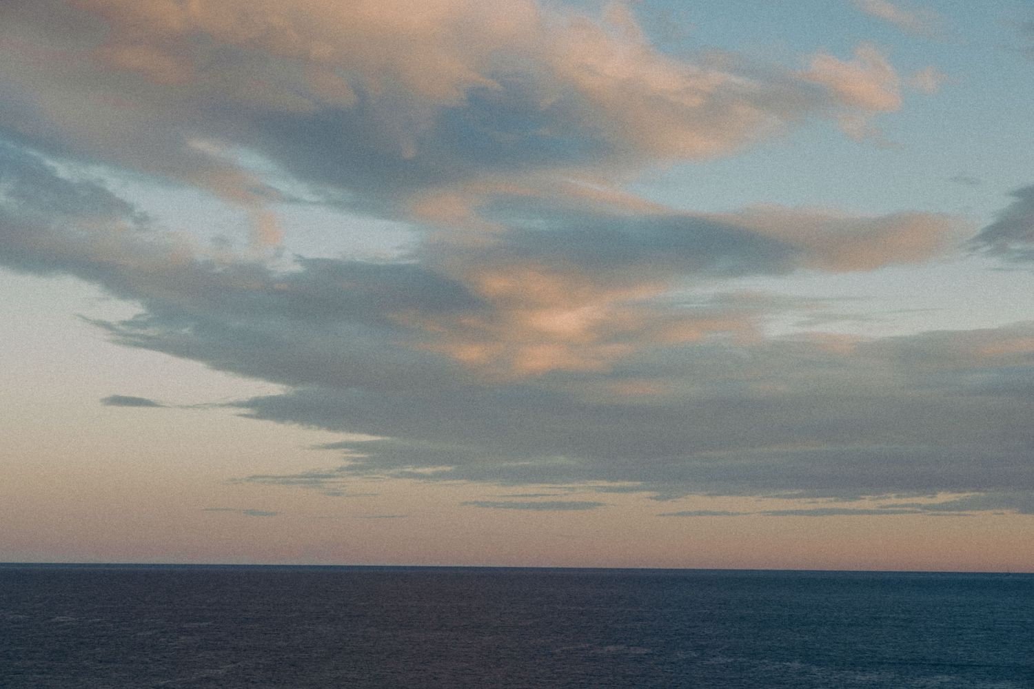 Panoramic view of a dramatic sunset sky with pink and blue clouds over a calm ocean horizon.