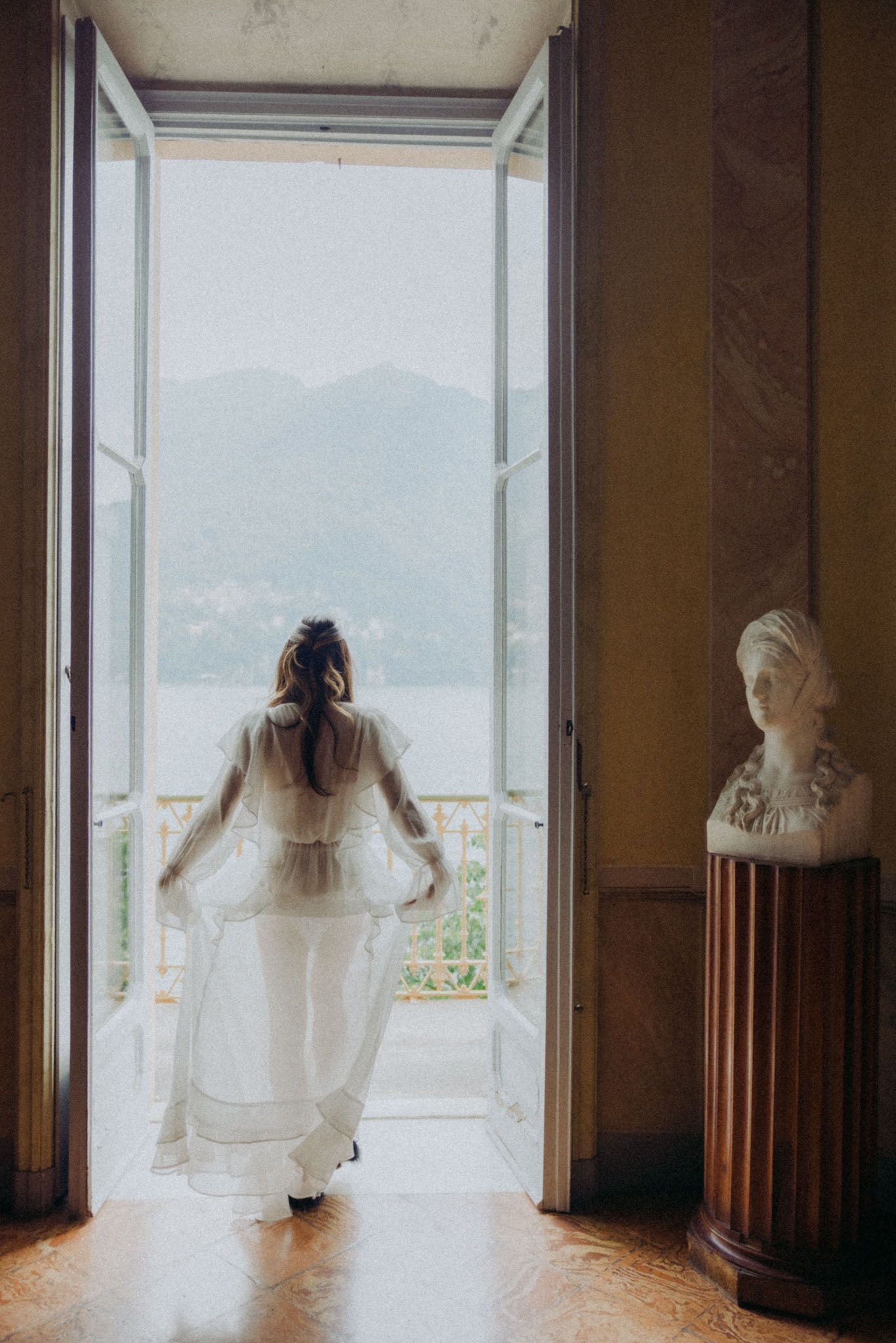 Multiple ethereal bridal figures in white dresses stand against large windows creating a dreamy panoramic effect.