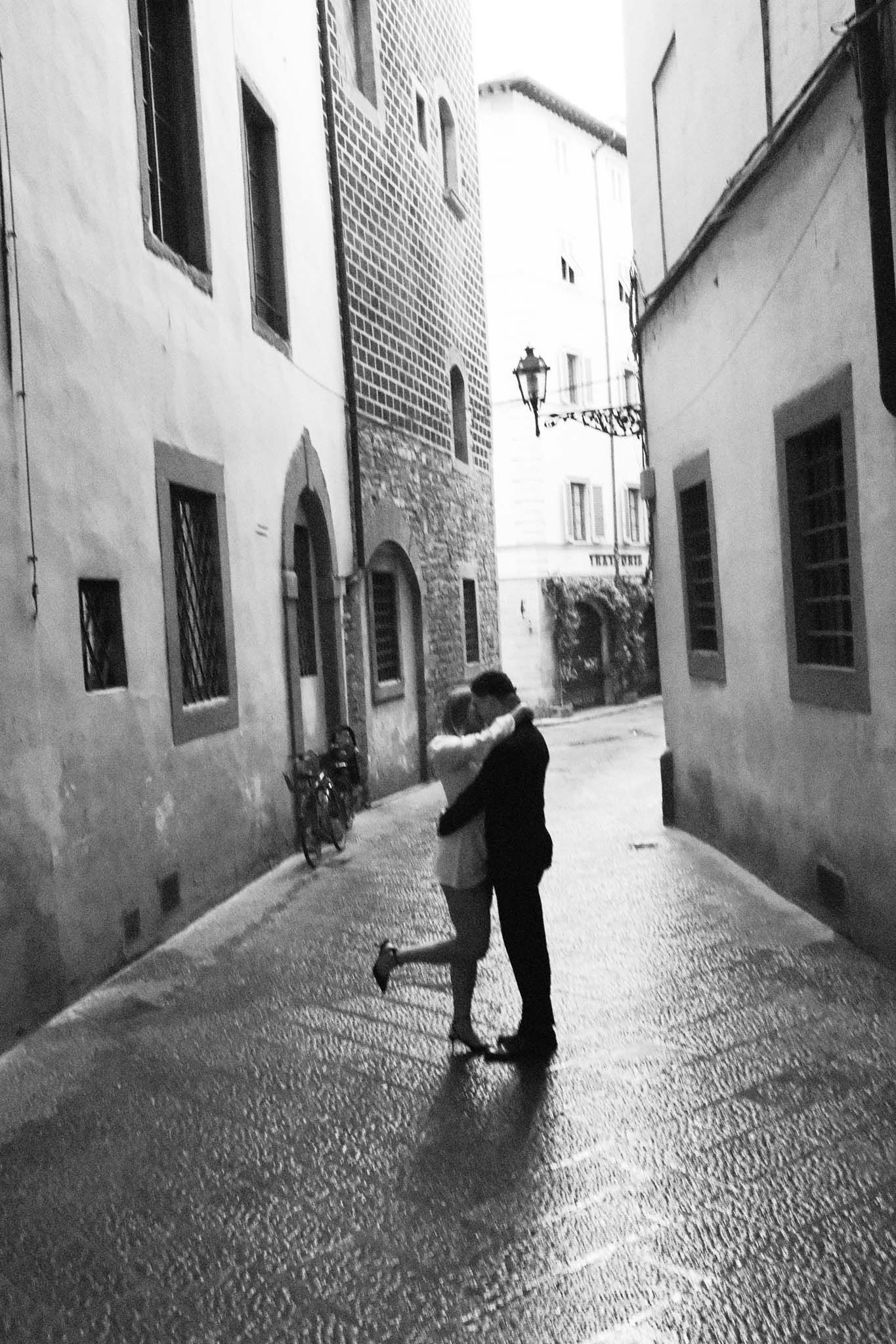A romantic silhouette of two people embracing in a narrow cobblestone alley of a European city.