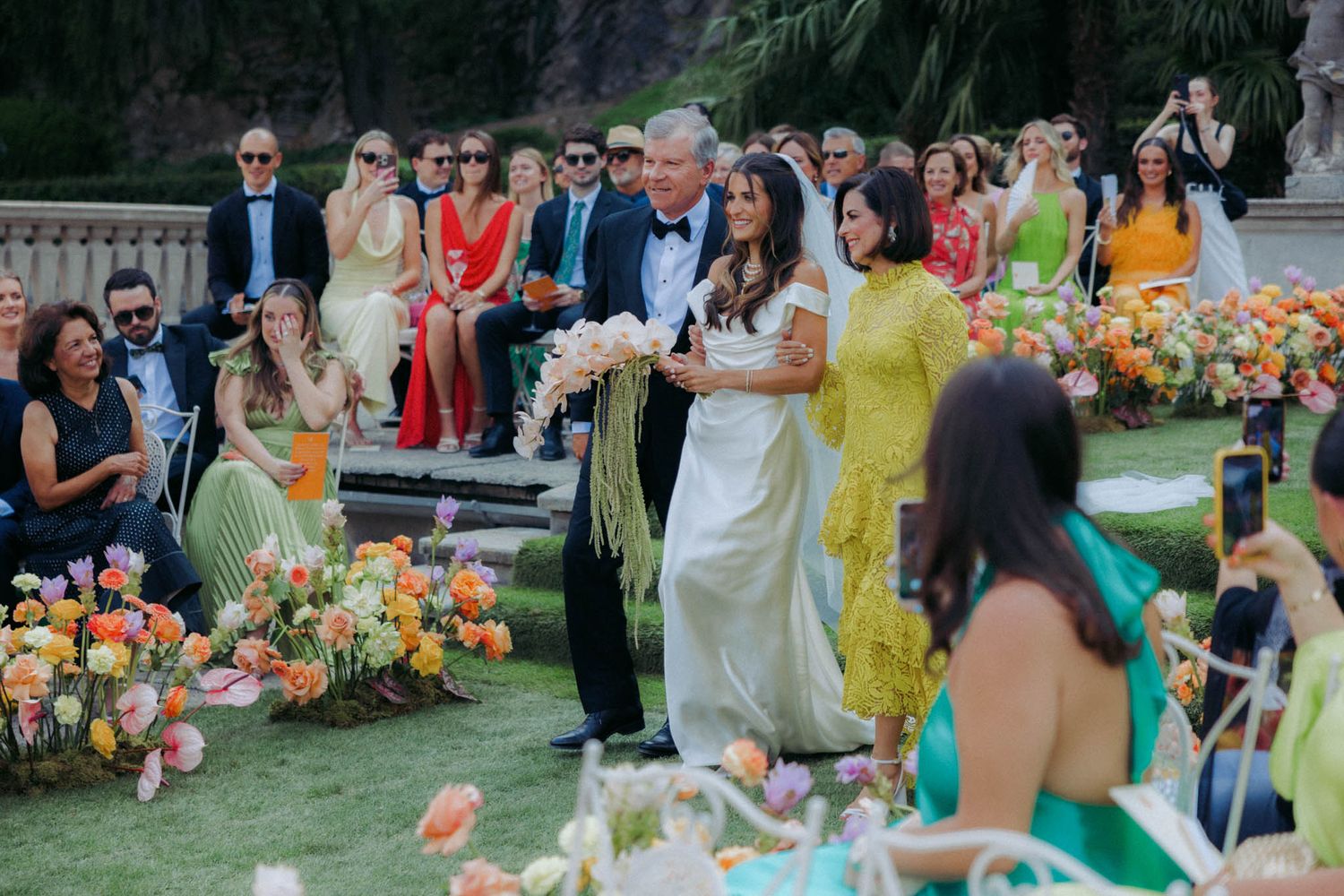 Wedding guests gather outdoors for a colorful summer celebration with vibrant floral decorations and tropical decor.