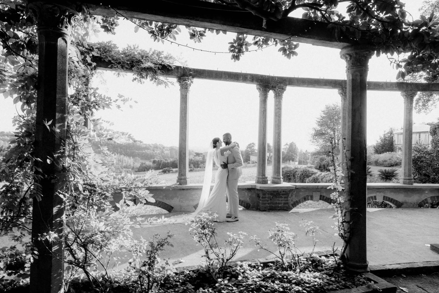 A panoramic black and white photograph shows a covered porch overlooking a scenic rural landscape with trees.