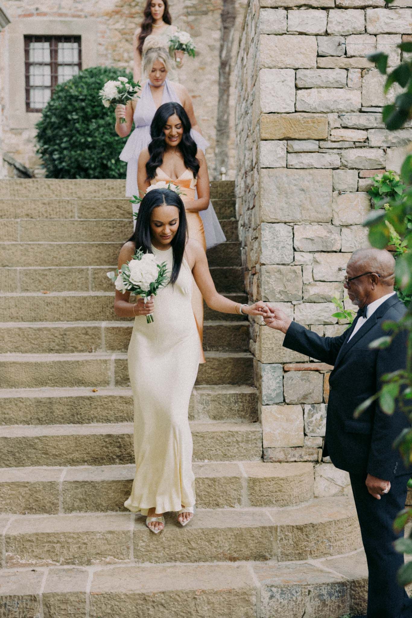 Bride in elegant white dress carefully descends stone steps during outdoor wedding ceremony.