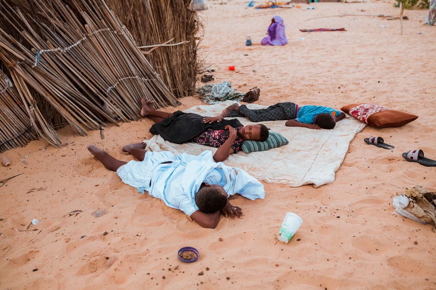 People resting on blankets in shaded desert camp area.