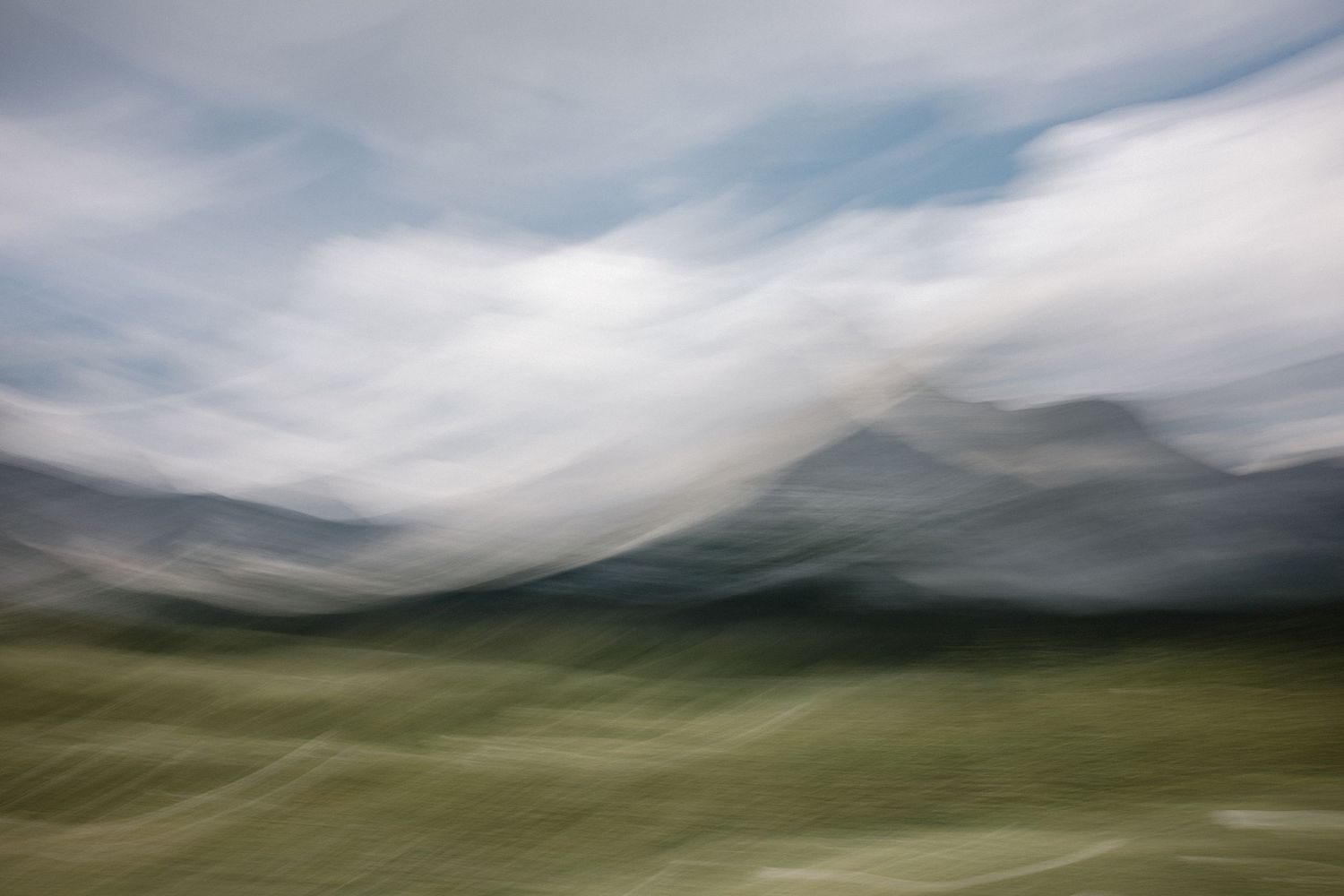 Blurred motion landscape photography shows rolling green hills and mountains under a cloudy sky.