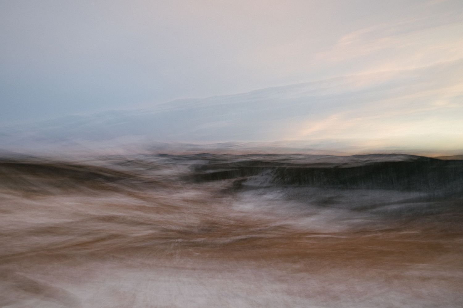 Abstract landscape photograph with soft motion blur of hills, capturing a horizon at dusk with dramatic clouds and warm golden light.