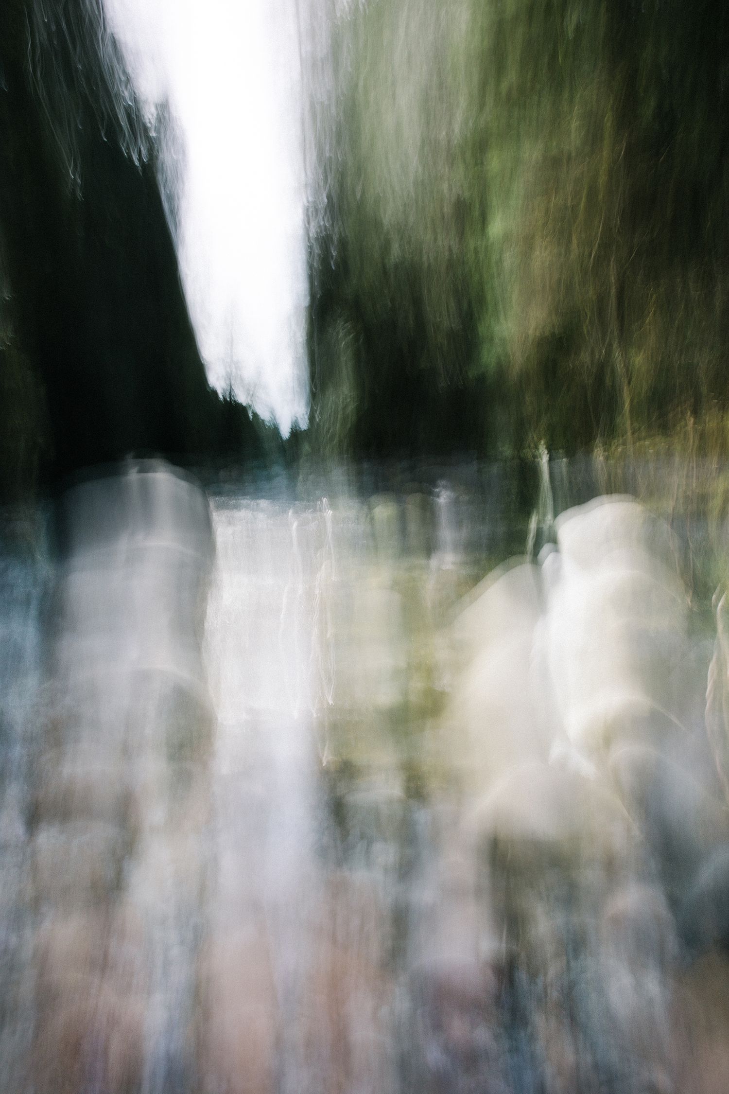 Abstract nature photograph with vertical motion blur, blending forest light, shadow, water reflections into a soft, atmospheric composition