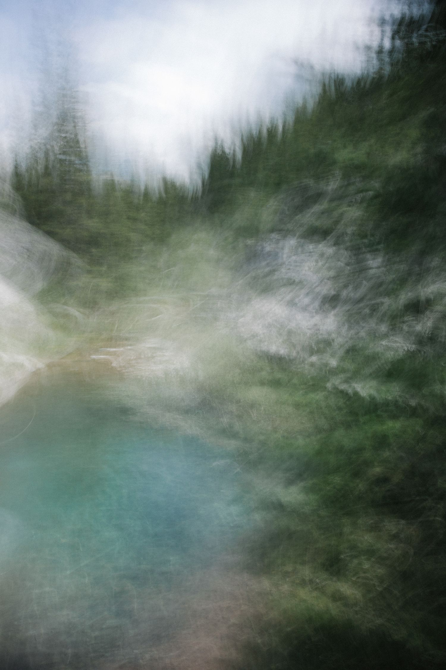 Abstract landscape photograph of a turquoise lake surrounded by blurred evergreen forest and gentle light.