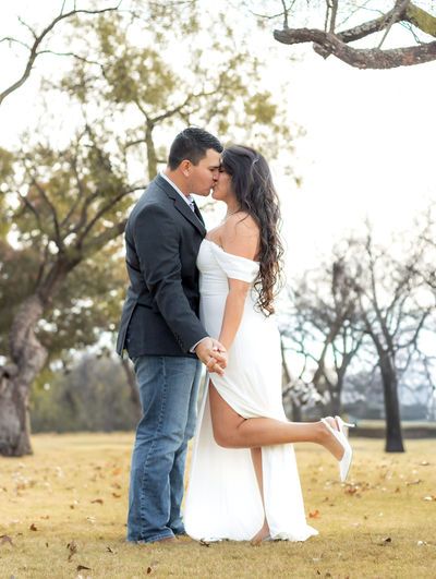 Couple sharing a kiss outdoors in white dress and dark blazer with jeans in autumn park.
