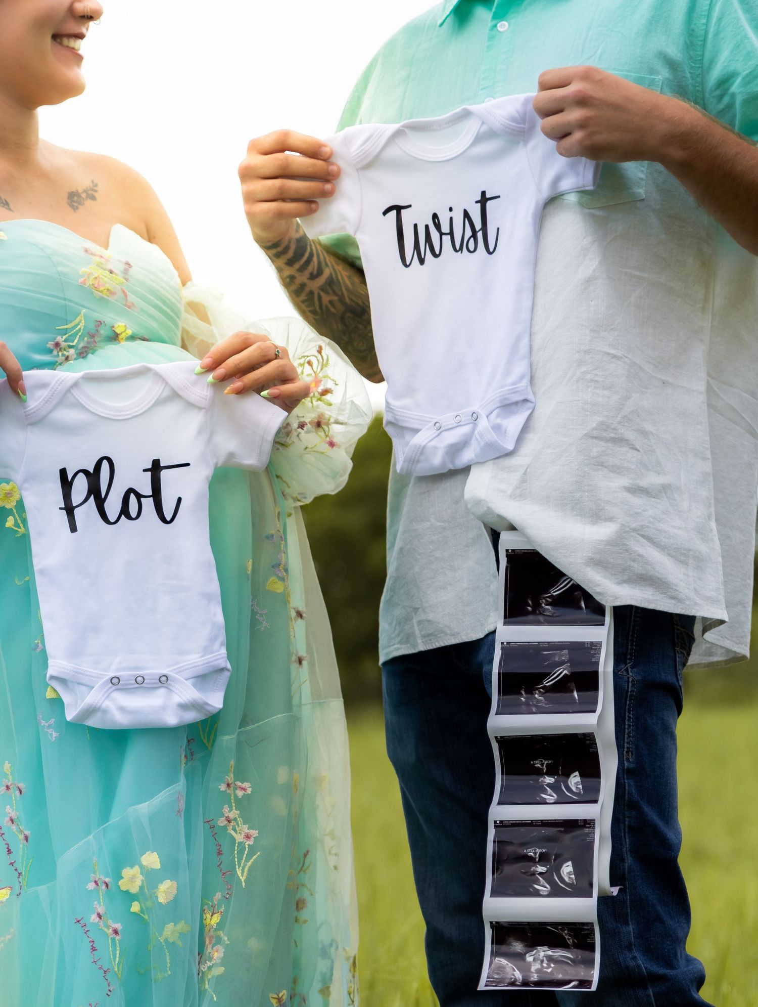 Expecting parents holding Plot and Twist baby onesies with ultrasound photos announcing twins.