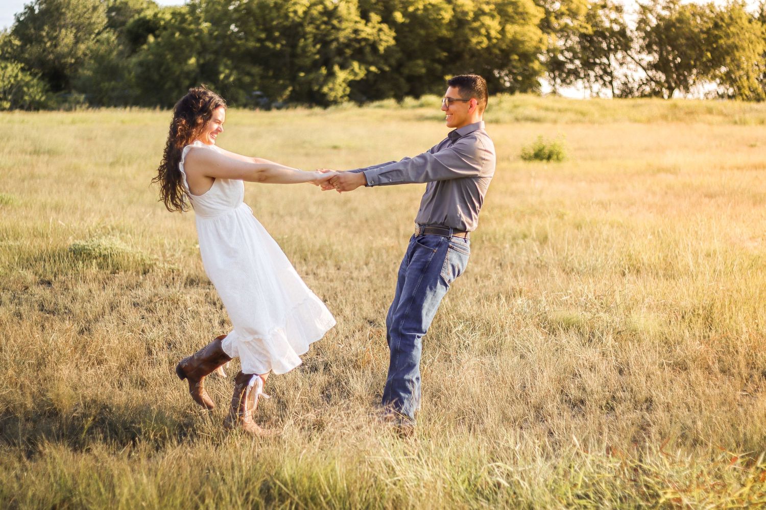 Couple dancing and spinning in sunny golden grass field, woman in white dress and cowboy boots.