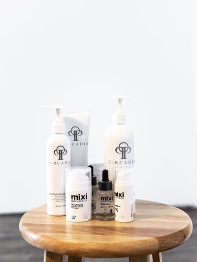 Circadia and Mixi skincare product collection displayed on wooden stool against white background.