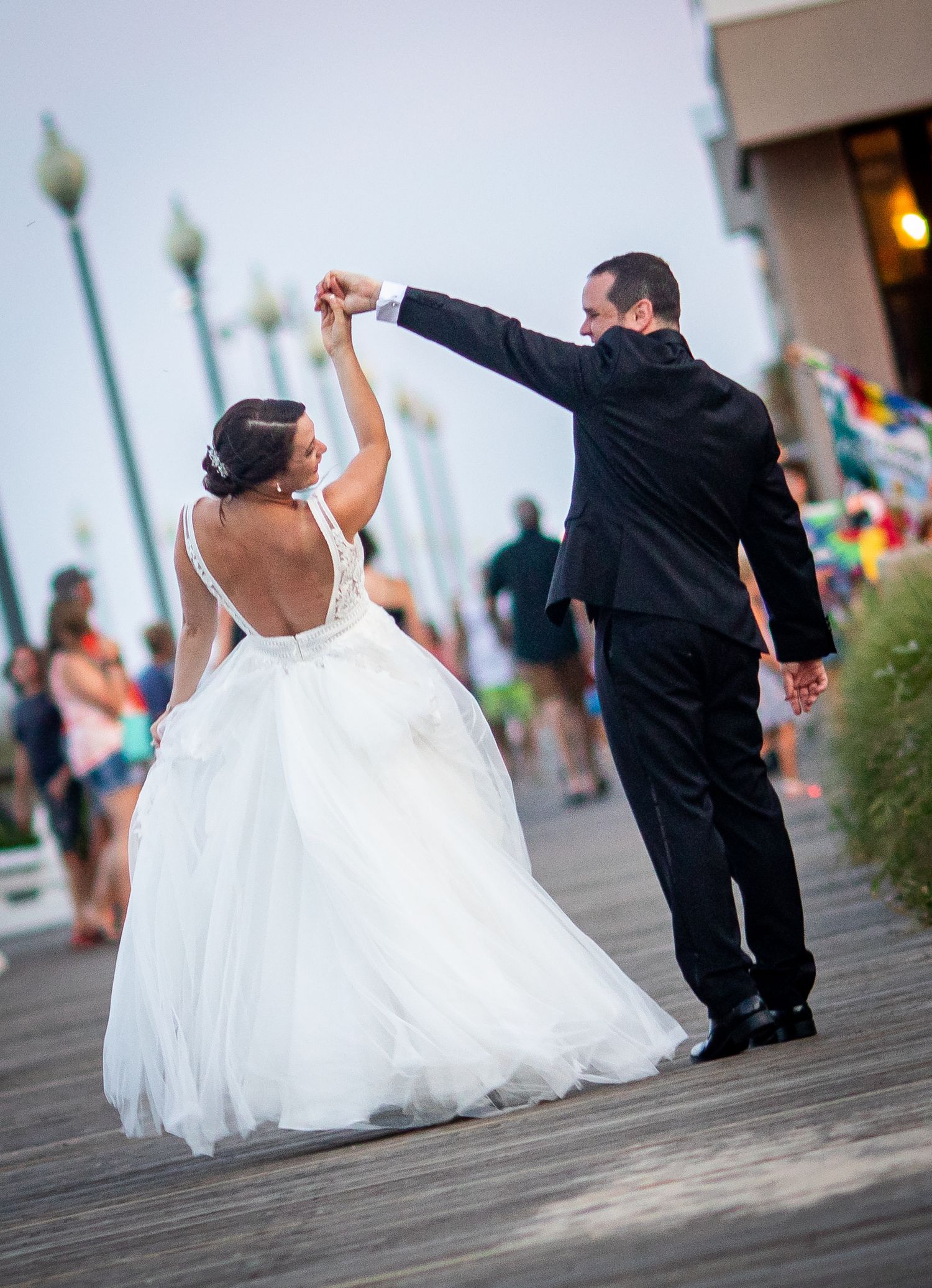 Wedding couple walking along a boardwalk in formal attire, bride's white dress flowing behind them.