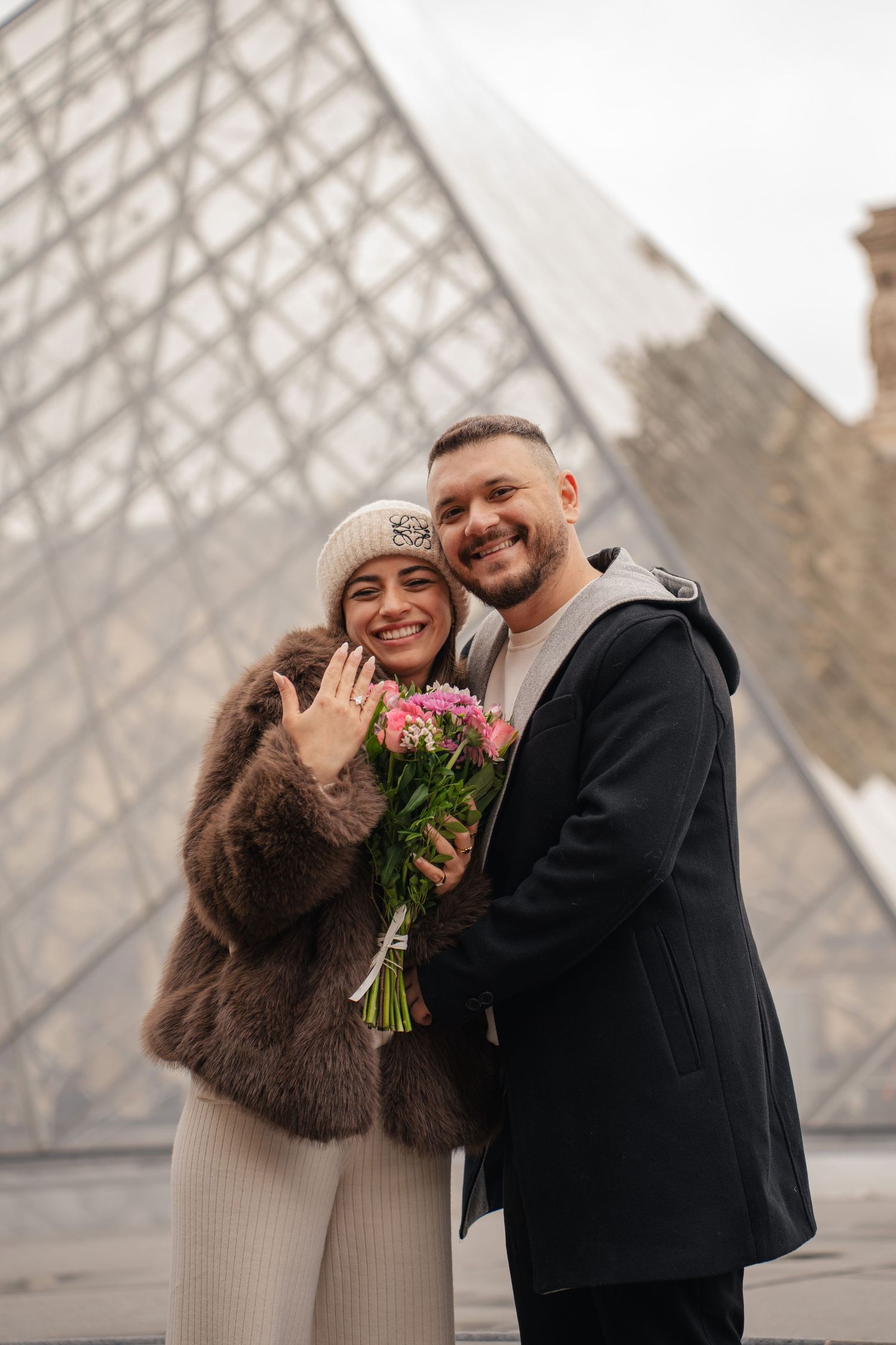 A romantic couple shares joyful moments in front of the iconic glass pyramid at the Louvre Museum in Paris.