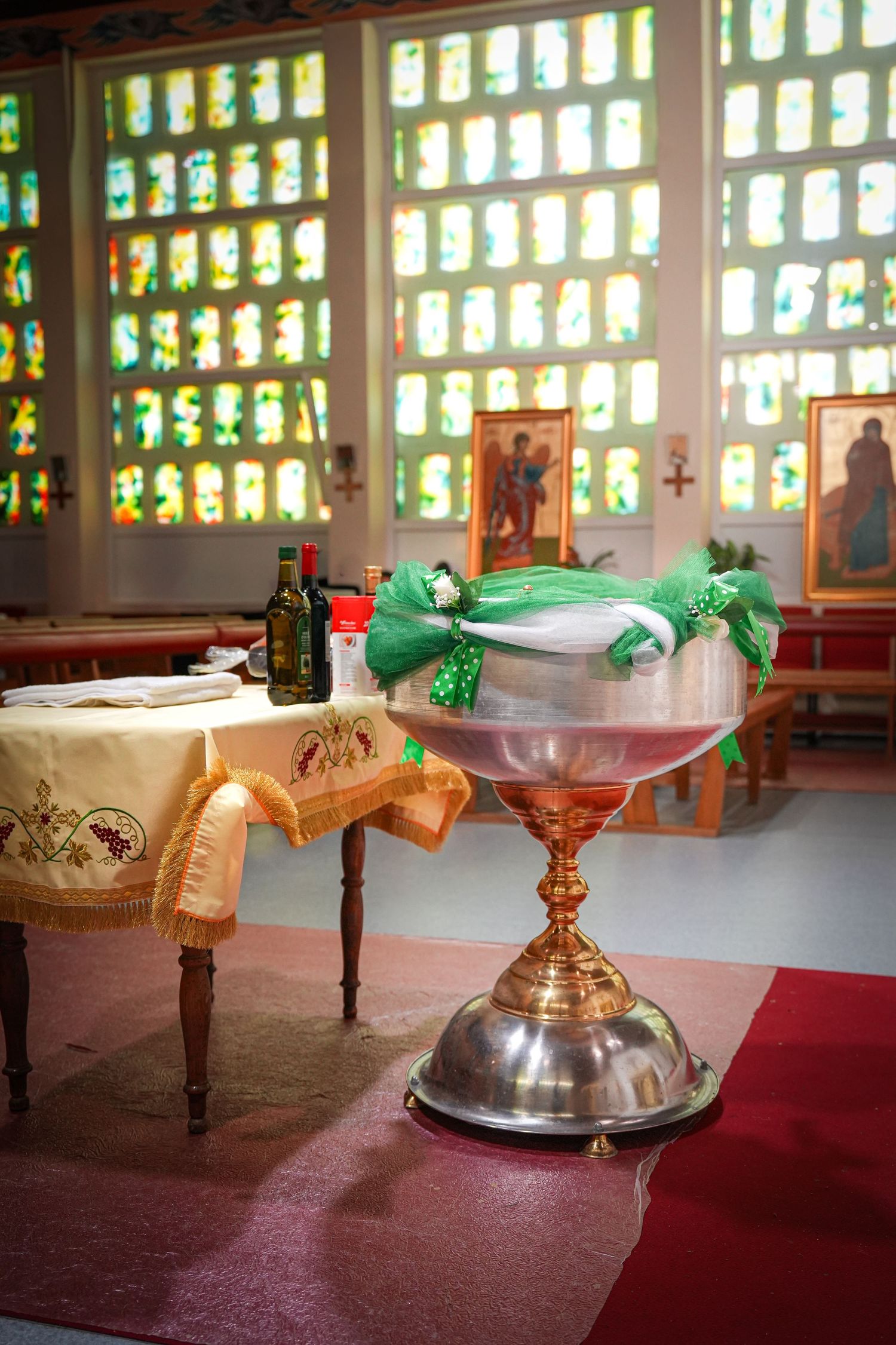 A large decorative glass bowl sits on a table with stained glass windows creating a colorful backdrop in a church setting.