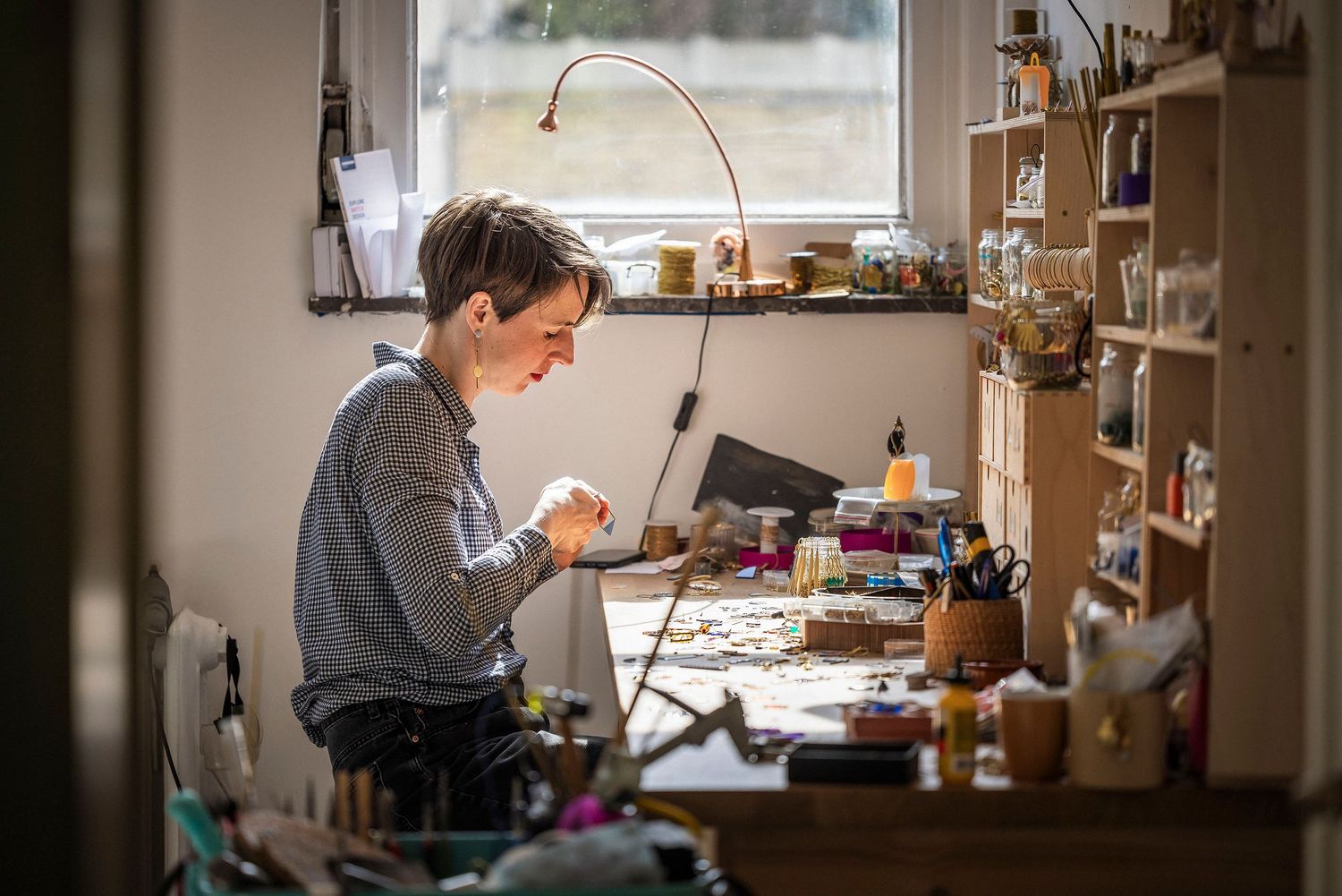 Sunlit workshop space with organized shelving and crafting supplies visible through large windows. Claire Bourguin Bourgain Bourgoin Bourqui
