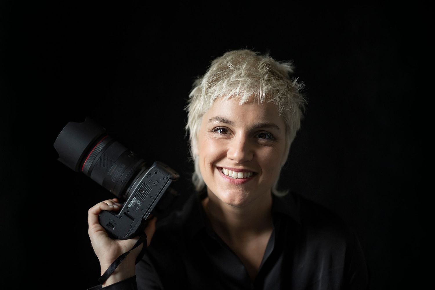 Portrait of photographer holding DSLR camera against black background.