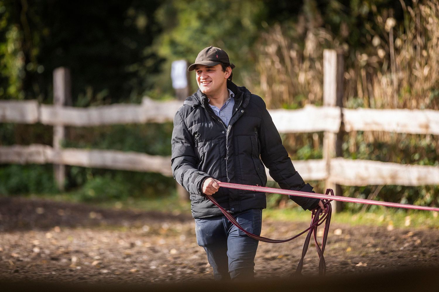 Person walking with a horse along a wooden fence on an autumn day.