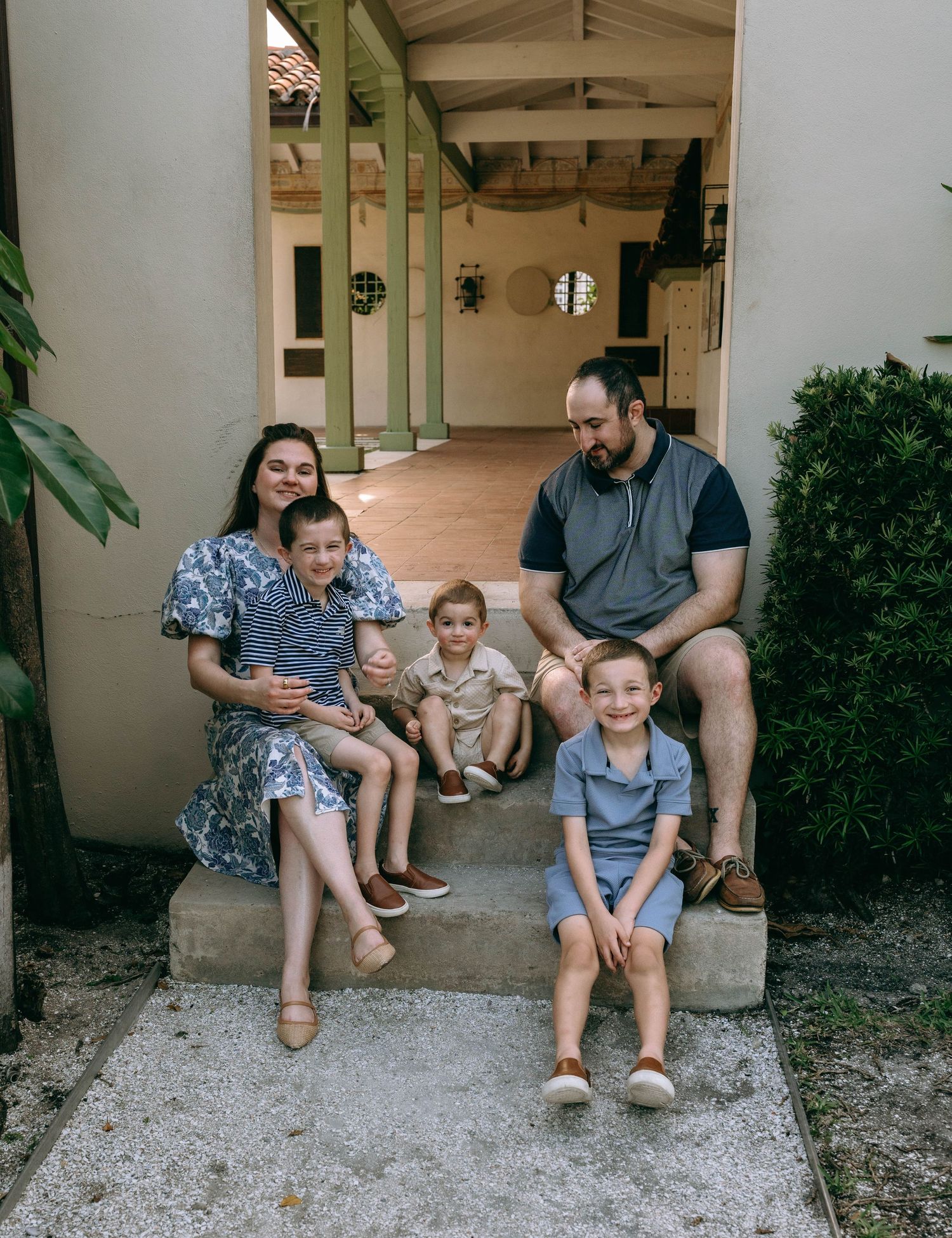 Family of five sitting on steps of a Mediterranean-style home entrance.  Family photos at Bradley Park Palm Beach, FL