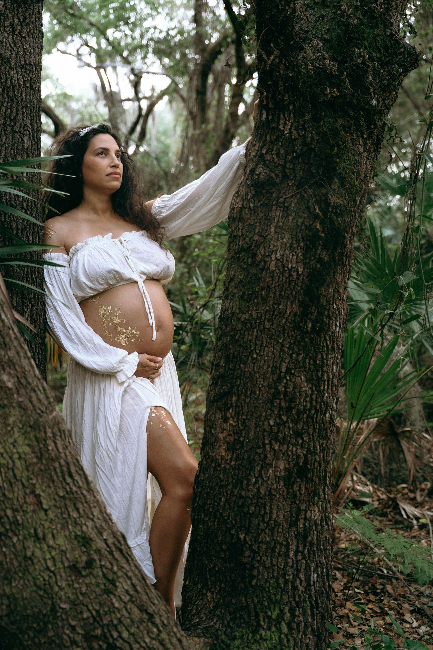 Forest maternity photoshoot featuring white peasant dress and natural lighting.