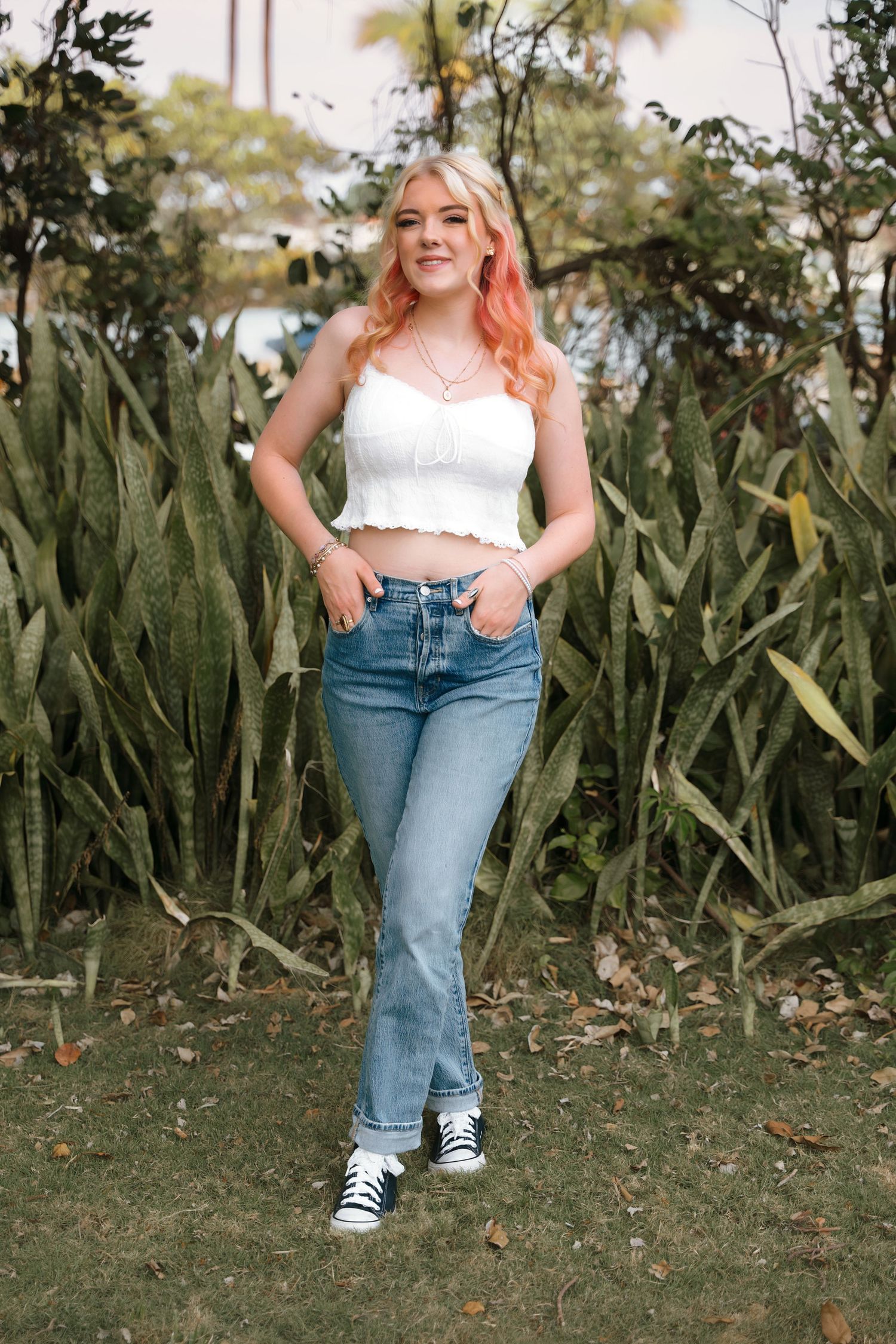 Casual outdoor photoshoot against green foliage wearing jeans and white crop top.