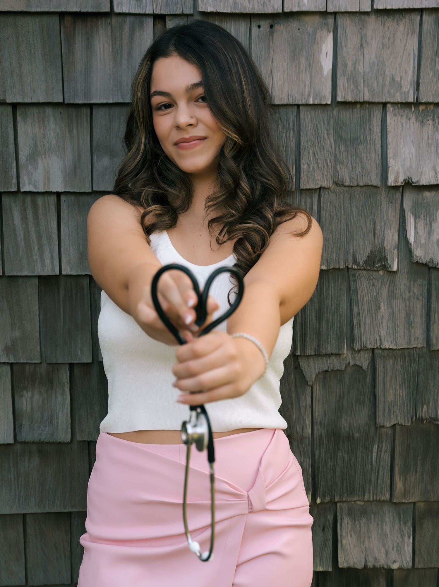 Fashion model poses against rustic wood shingle wall wearing pink and white casual outfit.