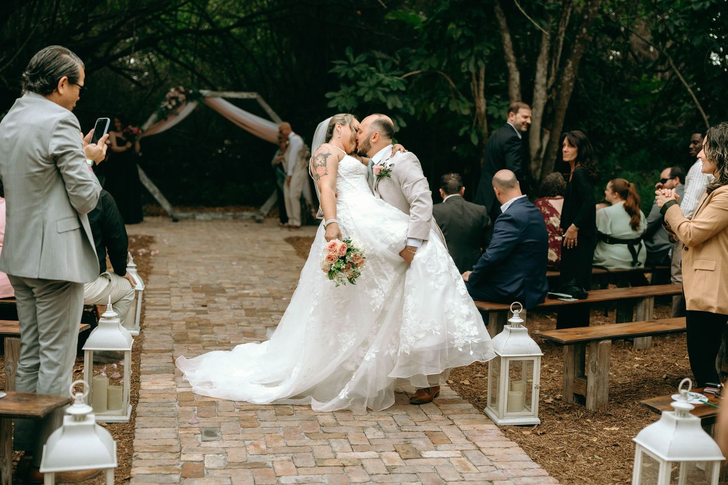 A couple shares a romantic dance at their outdoor wedding reception surrounded by guests and twinkling lights.