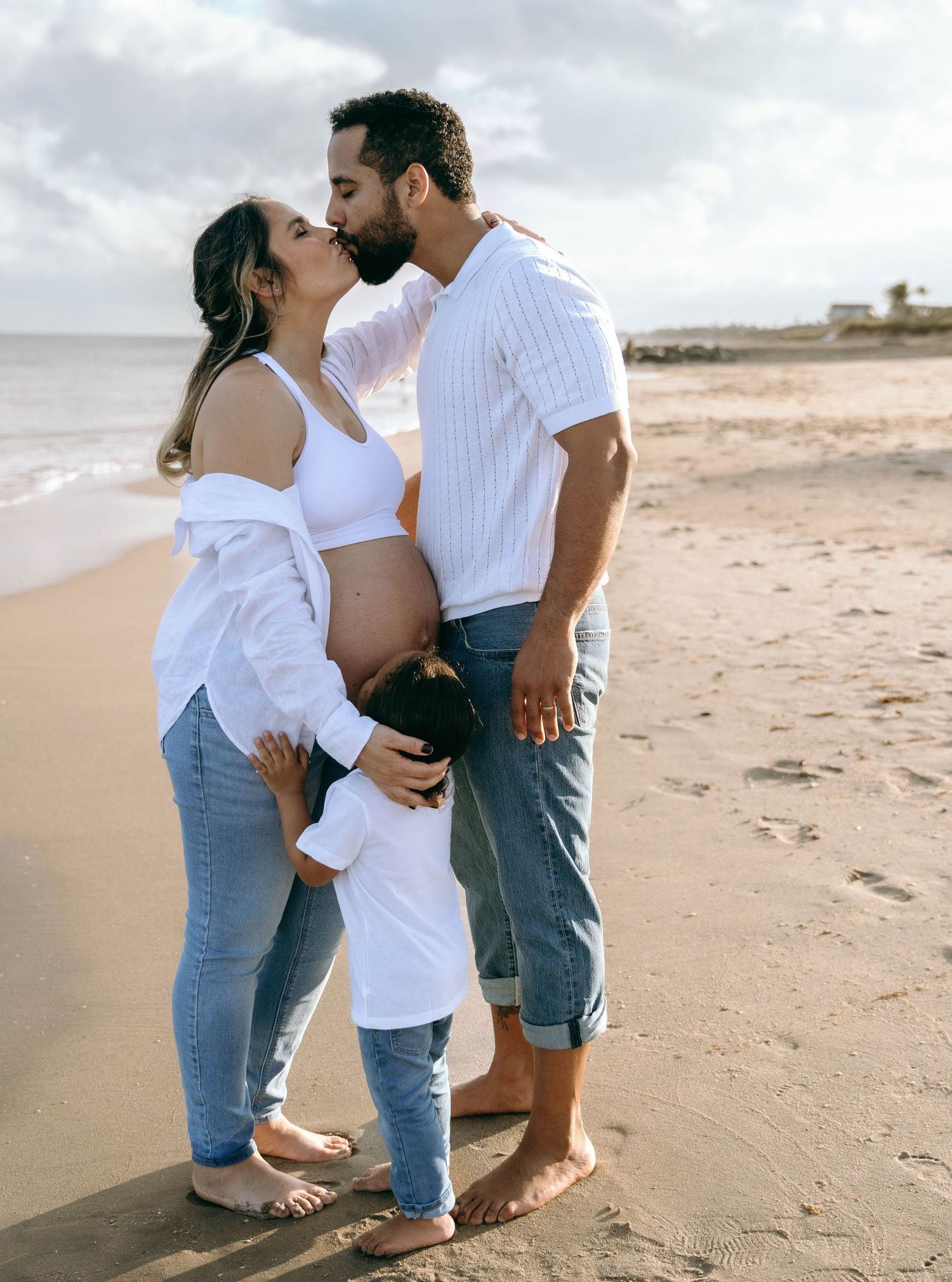 A couple in casual attire shares tender moments together on a sandy beach.