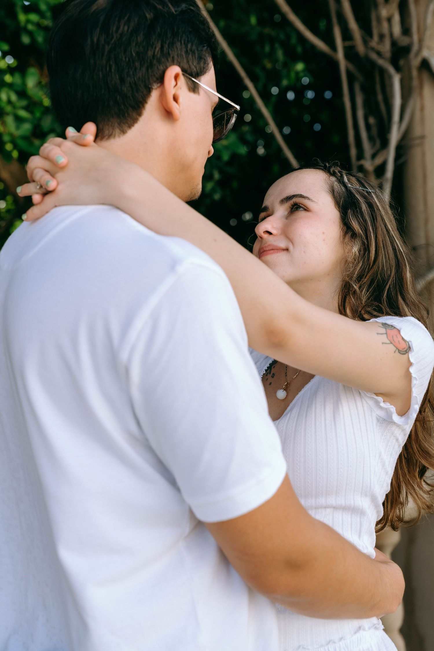 Romantic couple embracing outdoors, woman in white top looking up lovingly at man with glasses. Engagement photos on Worth Avenue