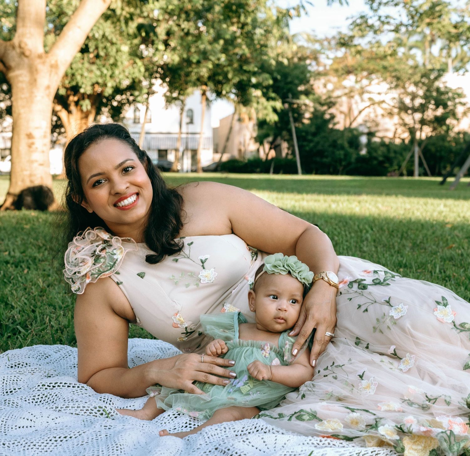 Family relaxing together on a white blanket in a sunny park.