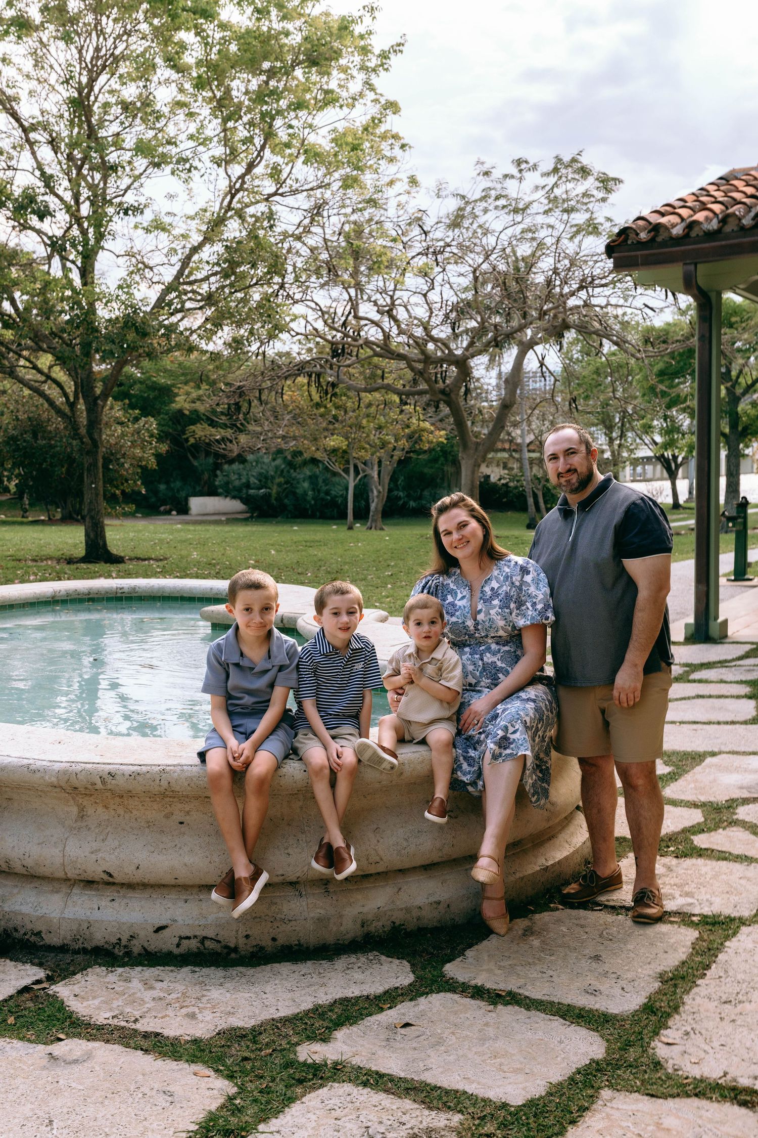 Family of five posing by a stone fountain in a lush garden setting.  Family photos at Bradley Park Palm Beach, FL