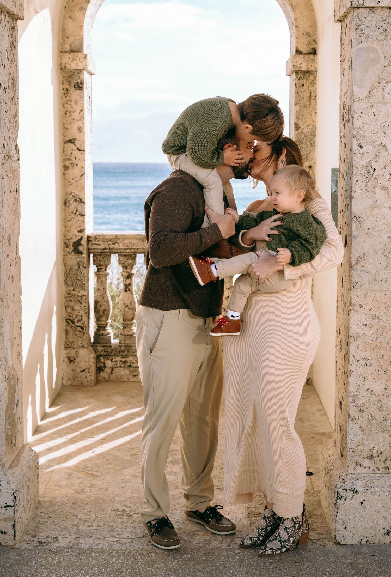 Family sharing intimate moment in stone archway overlooking ocean.