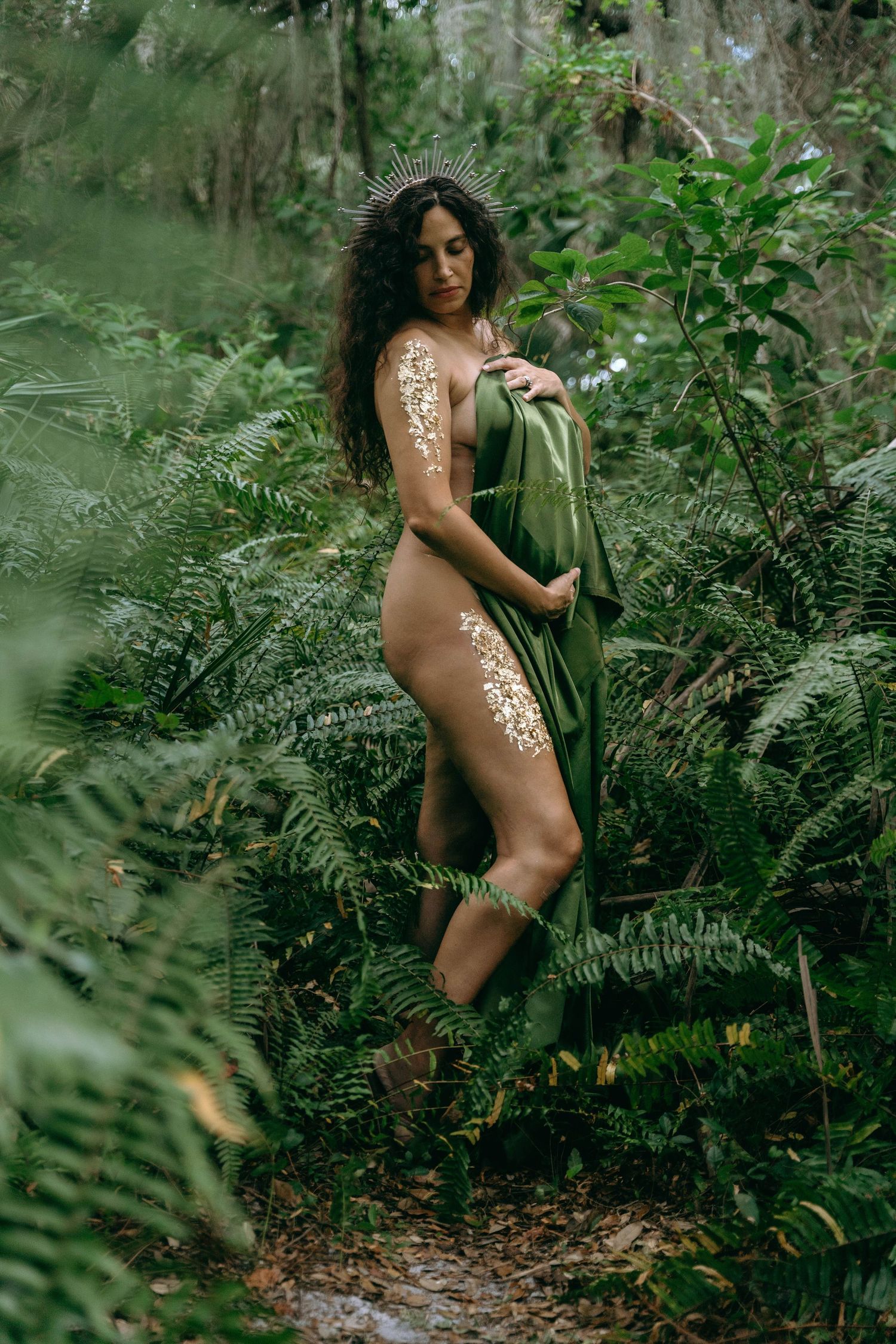 Artistic maternity portraits in green dress among lush forest ferns.