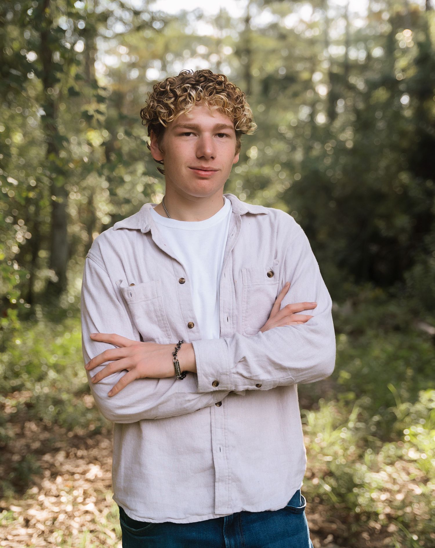 A person in casual attire poses against a sunlit forest background.