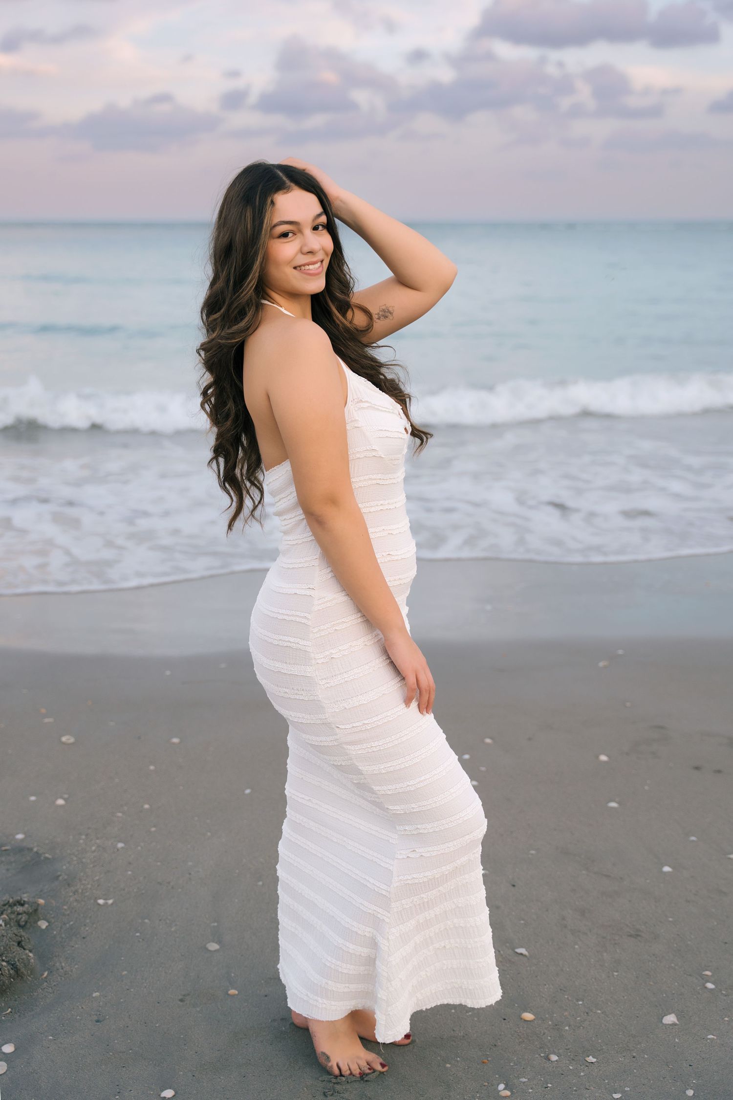 Beachside photoshoot featuring white summer dress against ocean waves.
