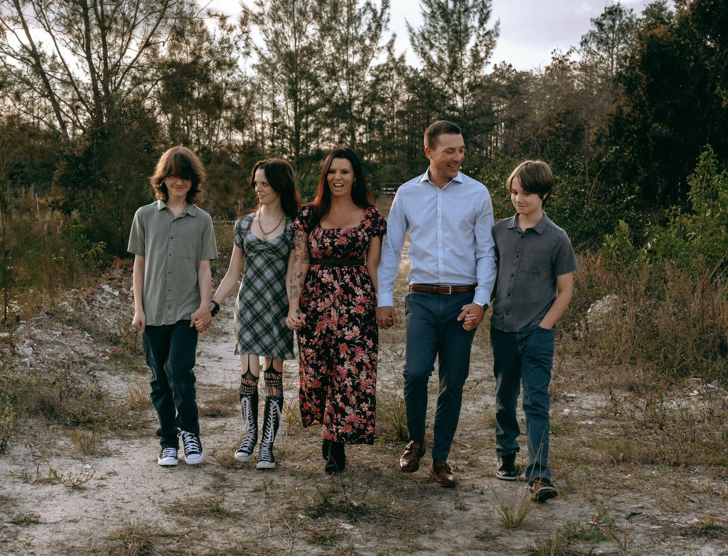 Family of five walking outdoors on sandy path surrounded by trees and shrubs during golden hour at Colt Farms in Boynton Beach FL..