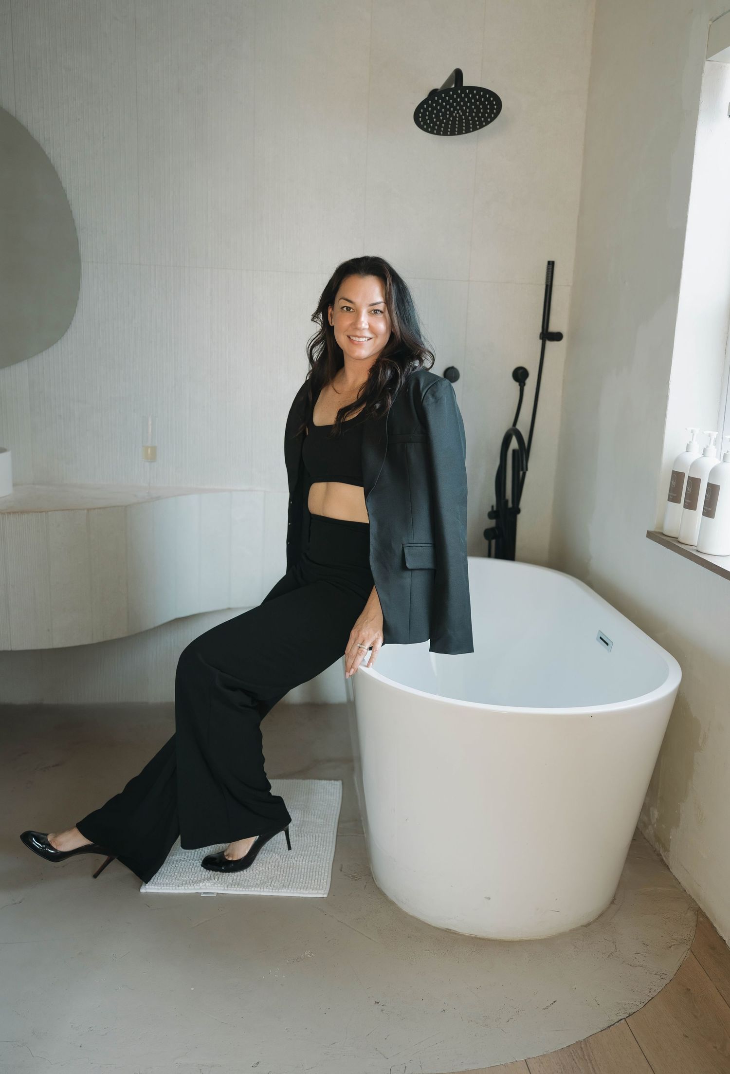Elegant bathroom scene with person in black outfit posing near white freestanding tub.