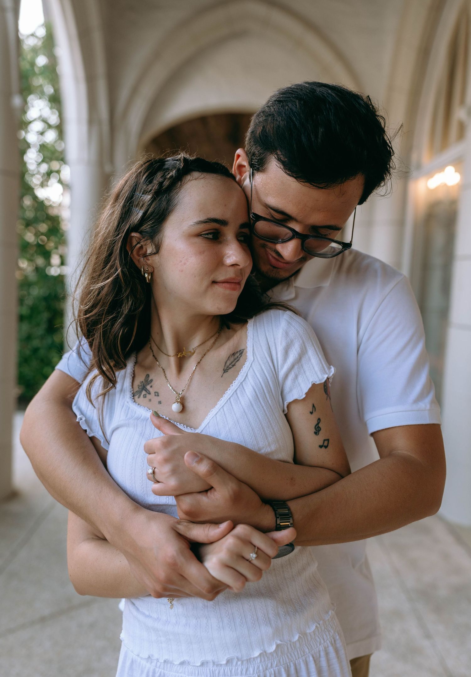 Couple embracing tenderly in an arched corridor, woman with tattoos leaning back into mans arms. Engagement photos on Worth Avenue