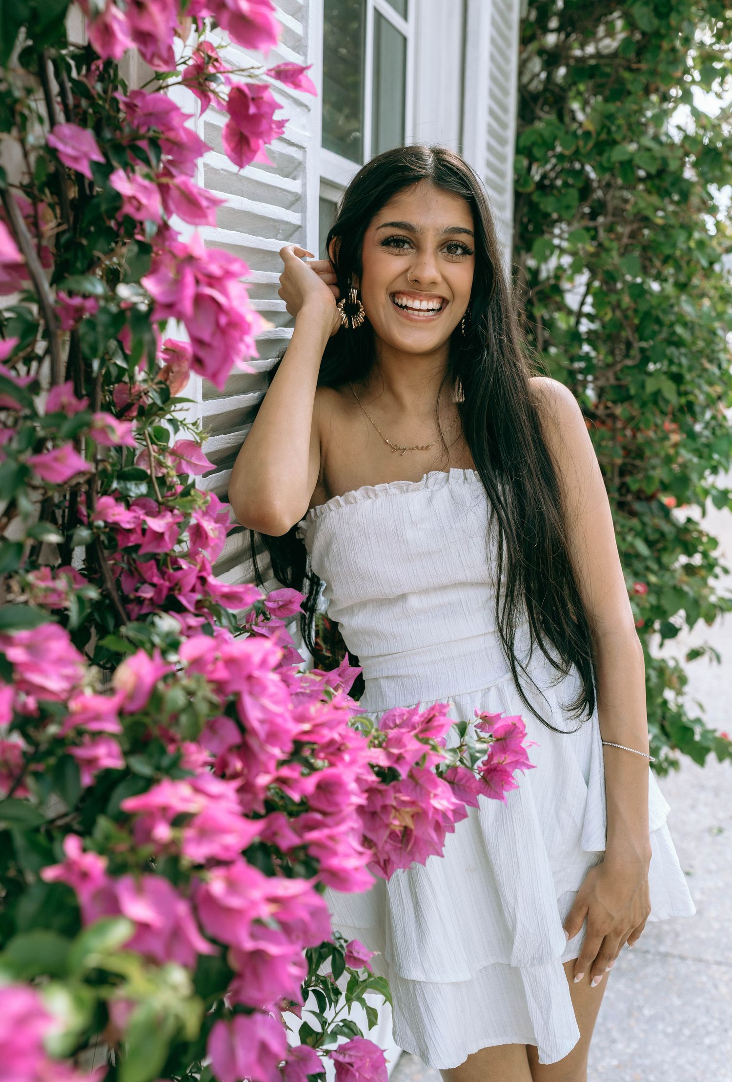 Smiling young woman in white strapless dress posing beside pink bougainvillea flowers outdoors on Worth Avenue Palm beach.