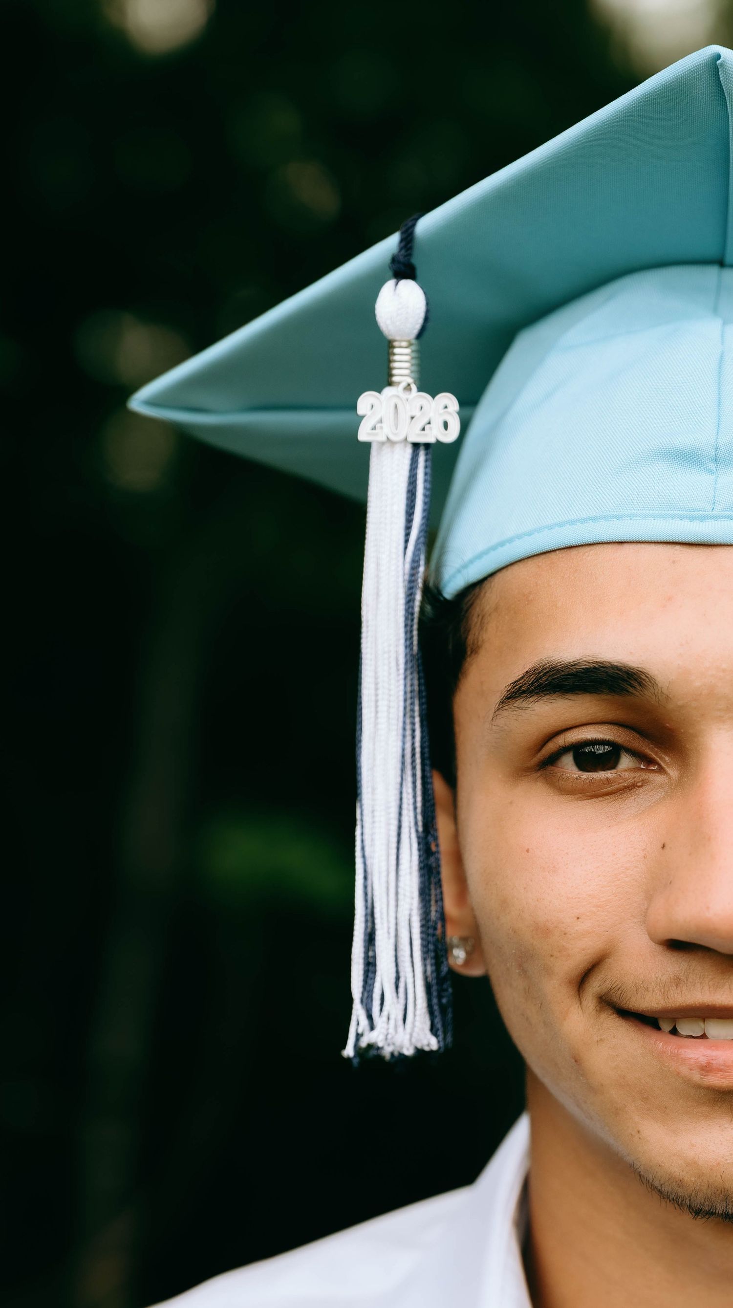 Smiling young man wearing a light blue 2023 graduation cap with tassel, celebrating his academic achievement outdoors. Senior Photos