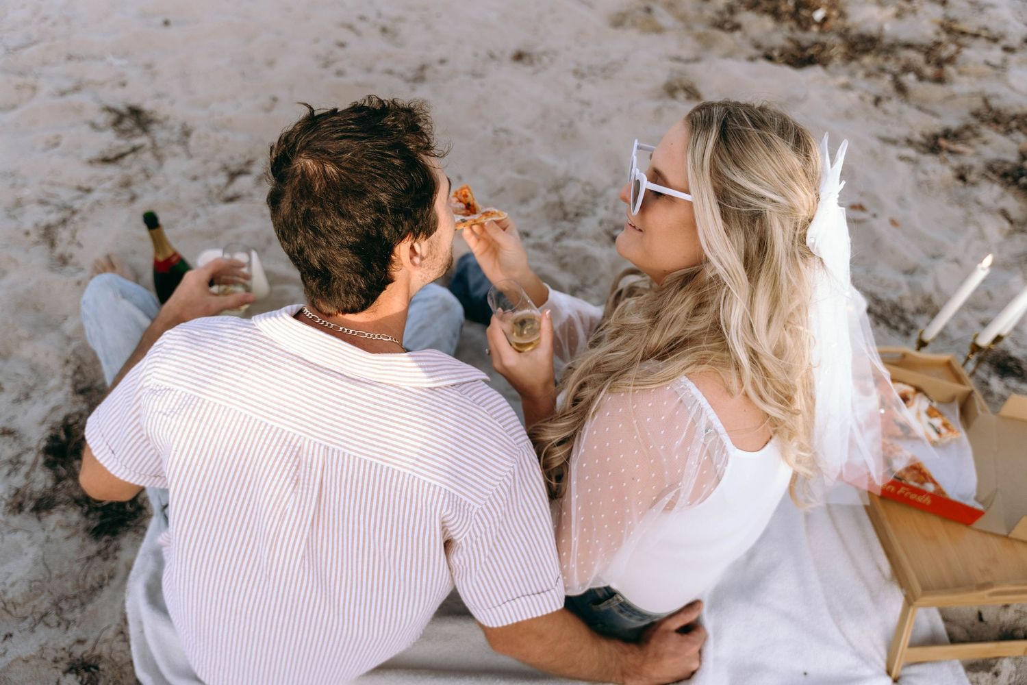 A couple shares a picnic on the beach with casual attire.