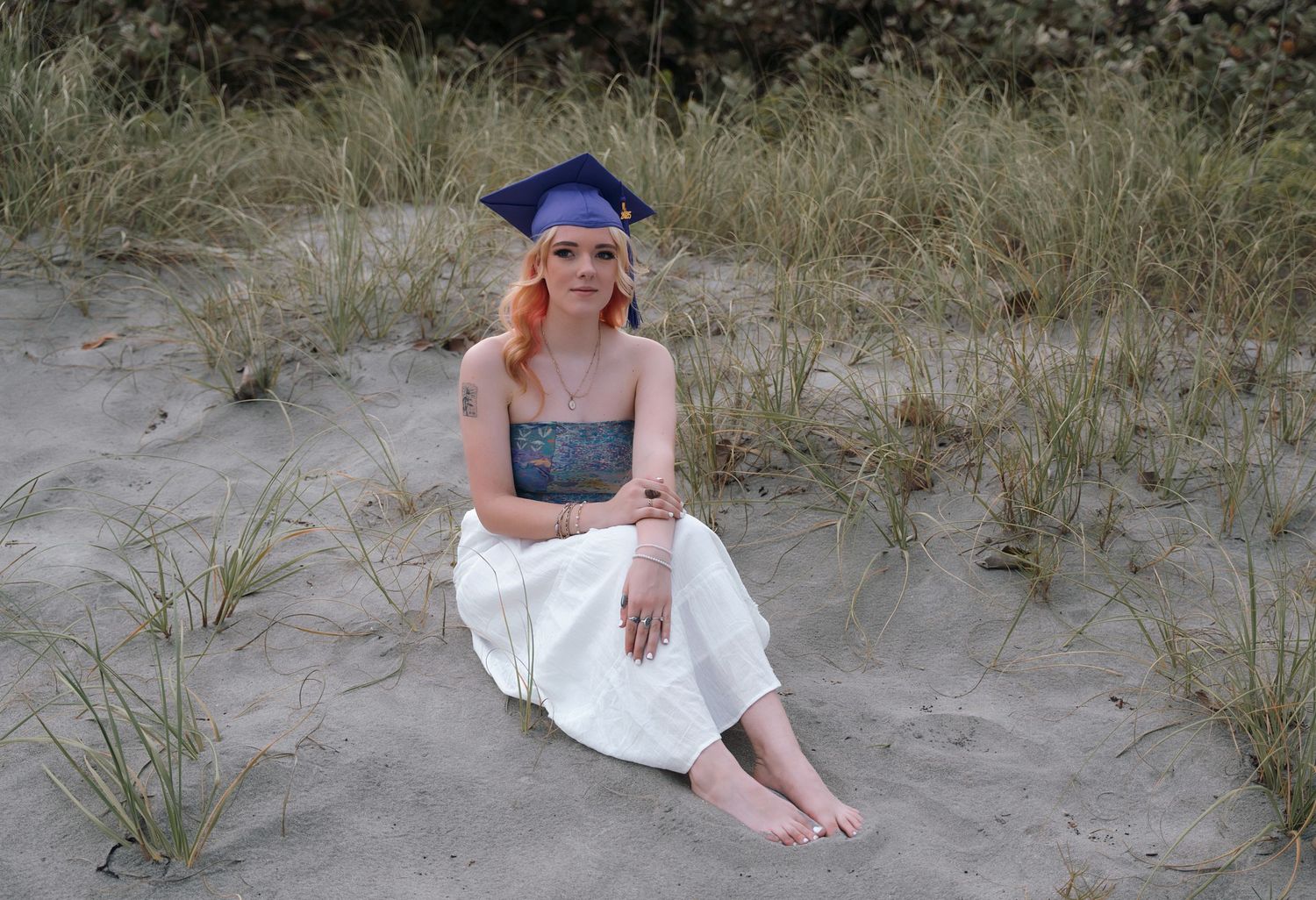 A beachy graduation photo taken in sand dunes with a blue cap.