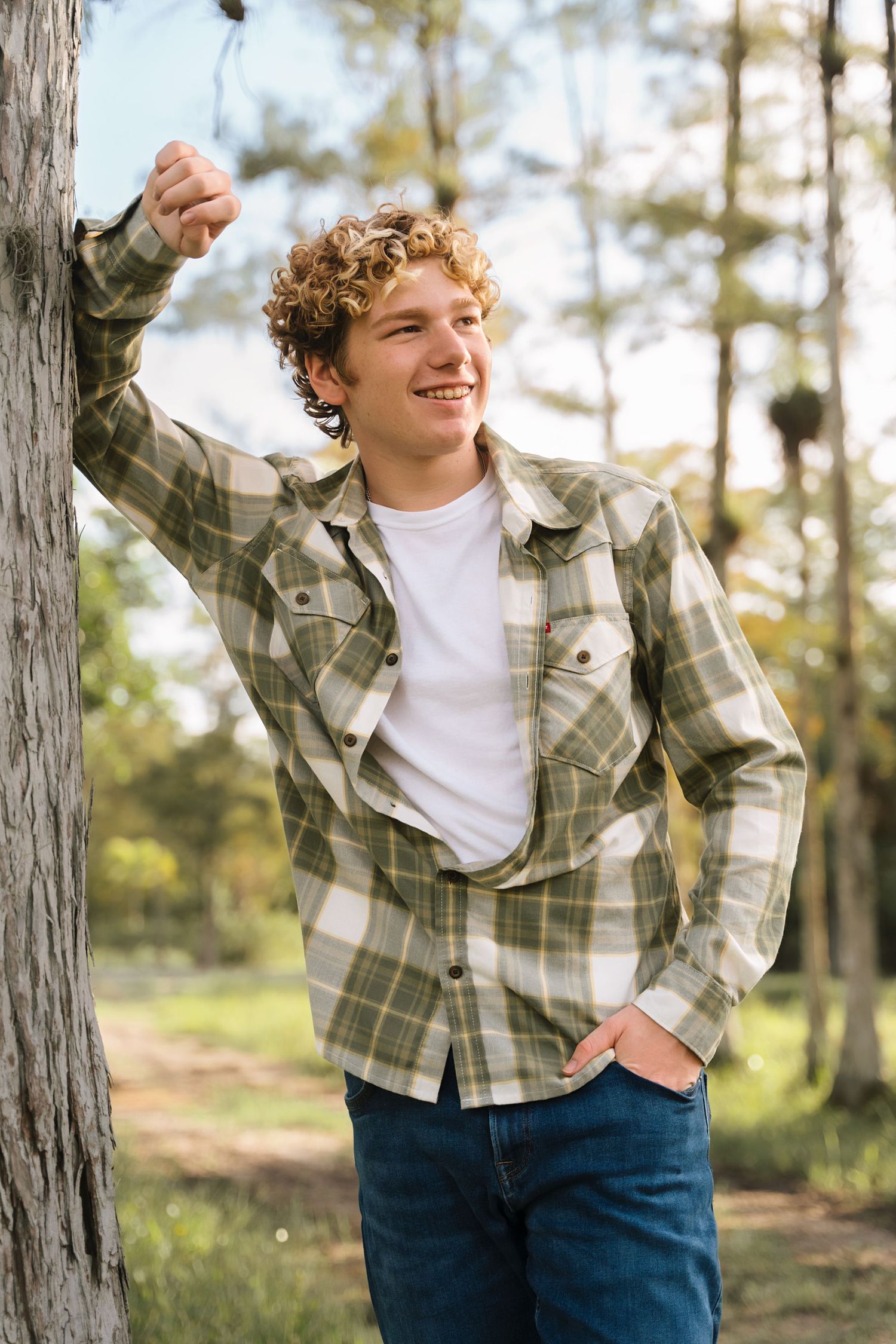 Playful poses in a natural setting wearing a plaid button-up shirt and jeans.